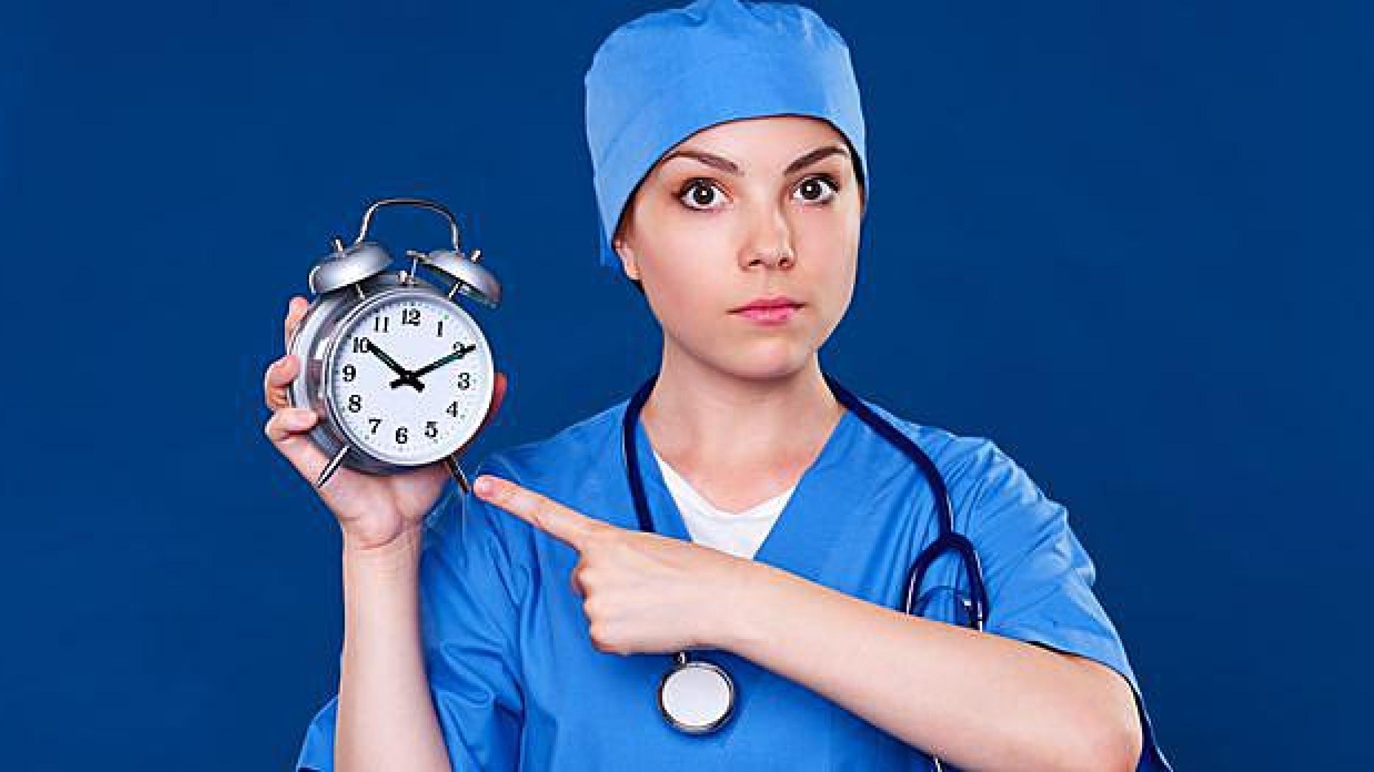 serious doctor pointing at alarm clock. studio shot over blue background