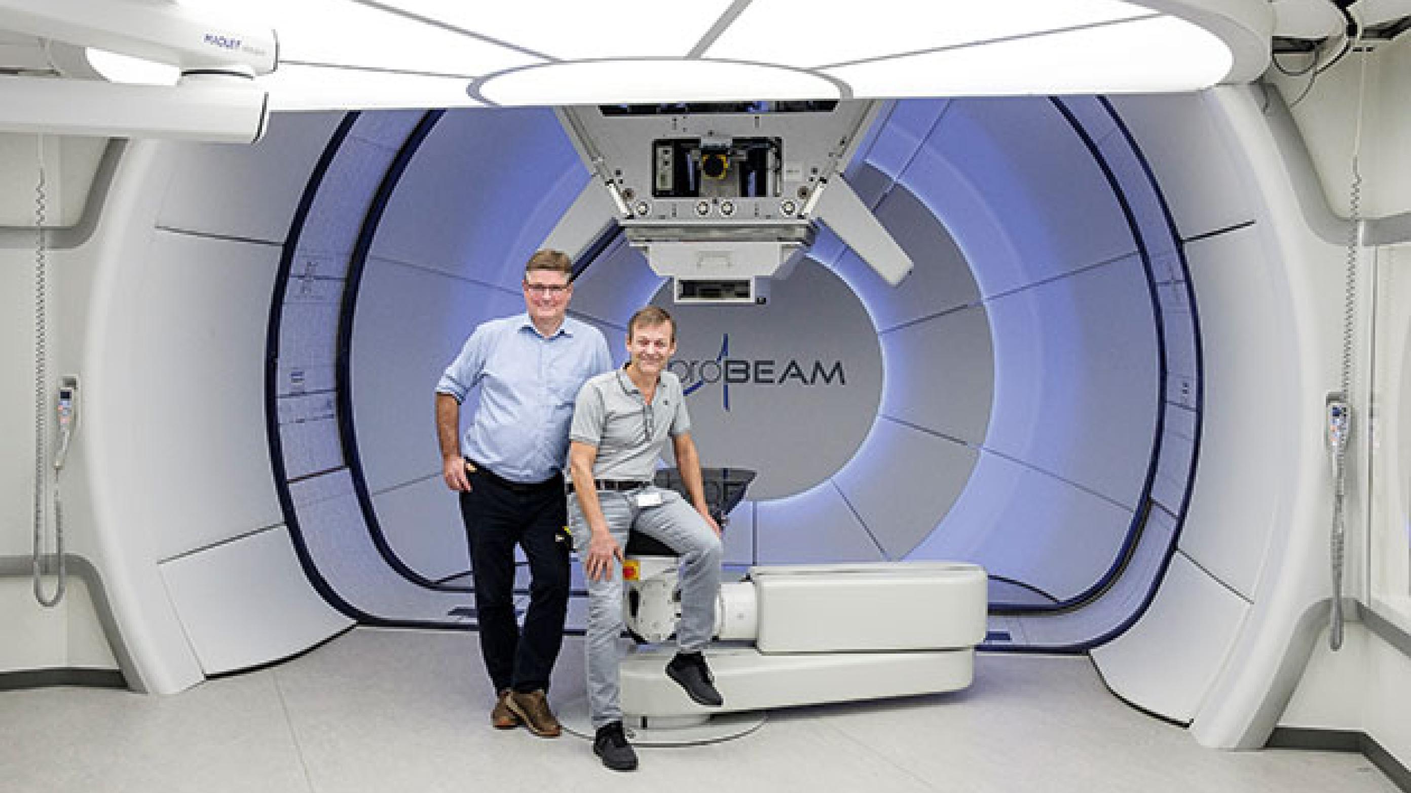 Professor, forskningsleder Cai Grau og ledende overlæge Morten Høyer i det ene af centrets tre behandlingsrum. Strålekanonen kan køre 360 grader rundt om patienten, der ligger på det sorte leje. Foto: Jesper Voldgaard.