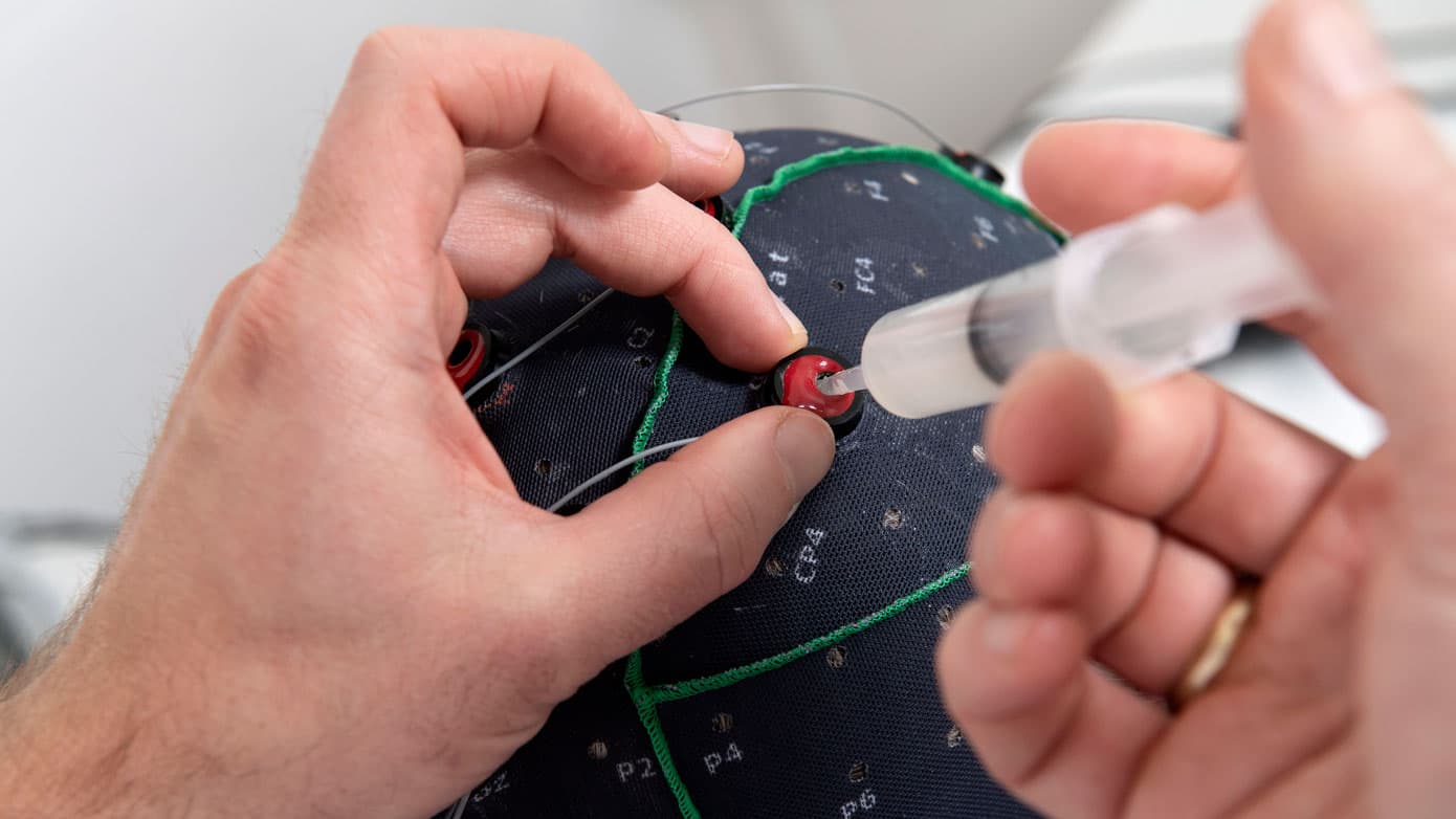 Patienten har fået en EEG-cap på hovedet. Nu sprøjter lægen en kølig gel ind gennem hullerne, som sikrer en bedre kontakt mellem elektroderne i hætten og kraniets overflade, og dermed en bedre overførsel af hjernens signaler. Lars Horn / Baghuset