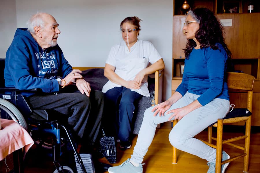 Mogens Bendiksen på 92 år taler med SOSU-assistent Anwar George og Anita Mink, der er på plejehjemmet en gang om ugen, under­viser personale og ser de patienter, der er behov for. Foto: Claus Boesen.