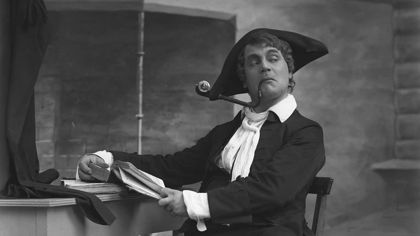 I sin mest berømte komedie gør Holberg nar ad de lærdes latin-snobberi. Studenten Rasmus Berg besøger sin landsby, Bjerget, hvor han blærer sig med sit latiniserede navn, Erasmus Montanus. Han har lært at disputere på latin, men kommer til kort, da han forsøger at imponere de jævne folk med sin indbildte store lærdom. Foto fra opførelse på Dramaten i Stockholm, 1910. Erasmus spilles af Anders de Wahl. (Wikimedia).