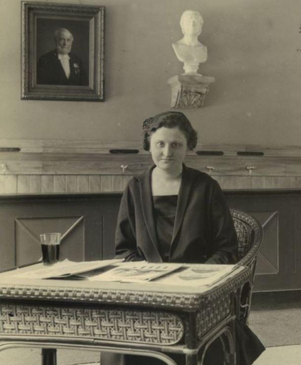 Billetdamen fru Barholt ved receptionen i Rosenborg Brøndanstalt, 1926. I baggrunden skranken med haner til forskellige mineralvandstyper. (Det kgl. Bibliotek)