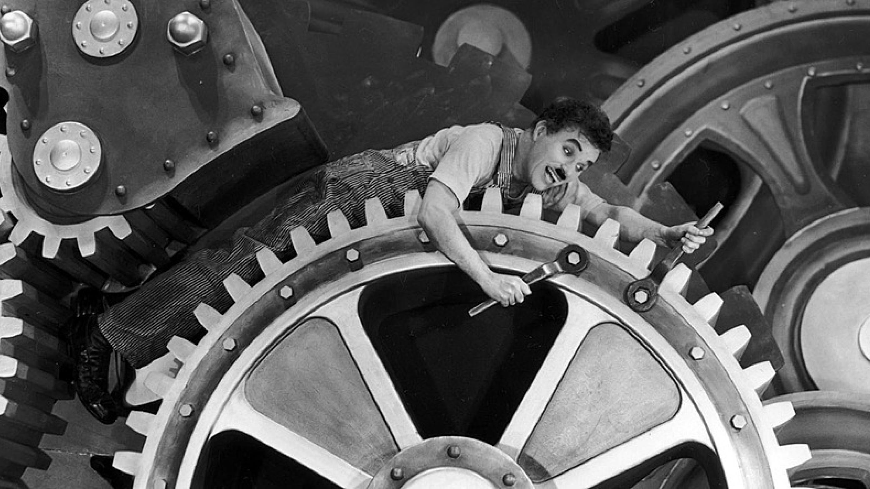 Charlie Chaplin bogstaveligt fanget i maskineriet i filmen "Moderne Tider" fra 1936. (c) Public Domain.