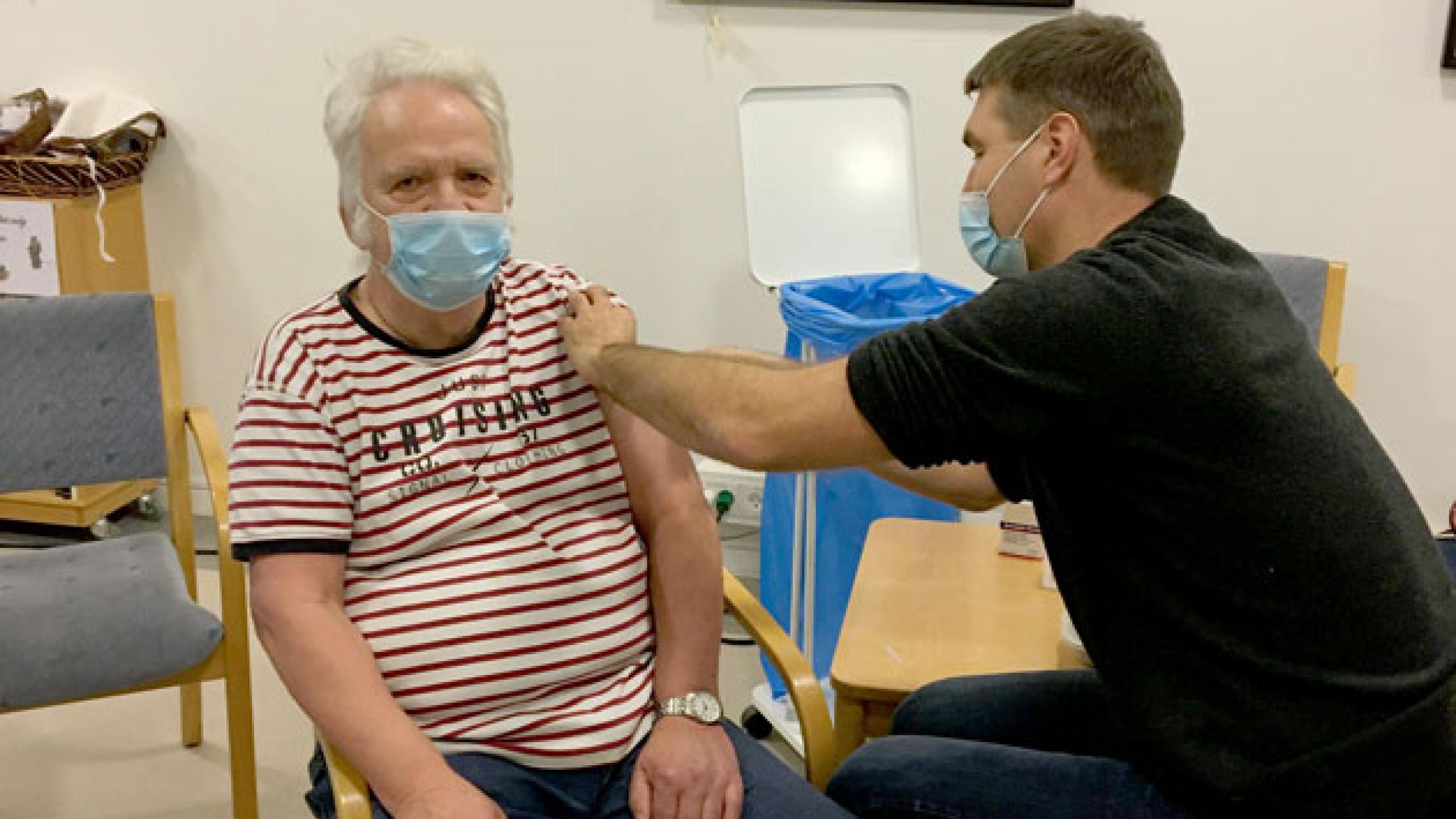 Med afsprittede hænder giver praktiserende læge Jonas Egdal plejehjemsbeboeren Leif den første vaccine. Foto: Privat 